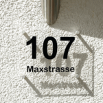 Hausnummer 3D in Schwarz mit Schattenwurf an Hauswand.
